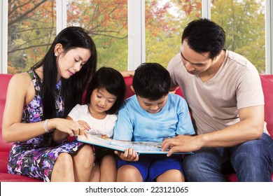 Hispanic Family Reading A Story Book Together On Couch With Autumn Tree Background