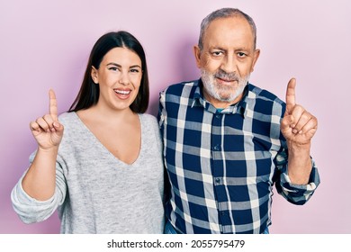 Hispanic Father And Daughter Wearing Casual Clothes With A Big Smile On Face, Pointing With Hand Finger To The Side Looking At The Camera. 