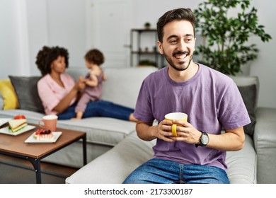 Hispanic Father Of Interracial Family Drinking A Cup Coffee Looking Away To Side With Smile On Face, Natural Expression. Laughing Confident. 