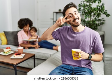 Hispanic Father Of Interracial Family Drinking A Cup Coffee Doing Peace Symbol With Fingers Over Face, Smiling Cheerful Showing Victory 