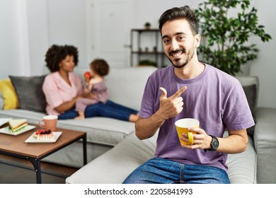 Hispanic Father Of Interracial Family Drinking A Cup Coffee Cheerful With A Smile On Face Pointing With Hand And Finger Up To The Side With Happy And Natural Expression 