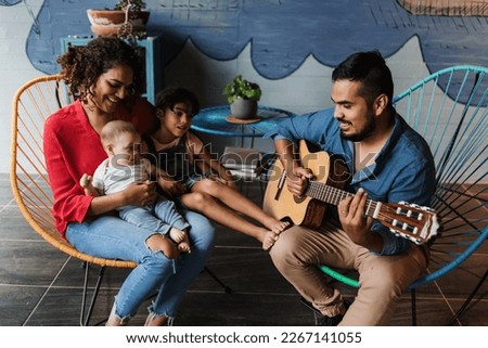 hispanic father playing guitar, singing and having fun with his family and daughter at home in Mexico Latin America