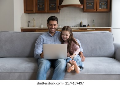 Hispanic father and preschool daughter sit on cozy sofa enjoy weekend with laptop, watch family movie, funny videovlog, laughing feels happy. Young generation use modern tech, leisure at home concept