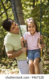 Hispanic Father Pushing Daughter On Swing.