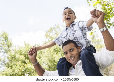 Hispanic Father And Son Having Fun Together Riding On Dad's Back In The Park.