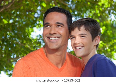 Hispanic Father And Teenage Son Happily Standing Together Outside In Yard, Looking Off Into Distance.