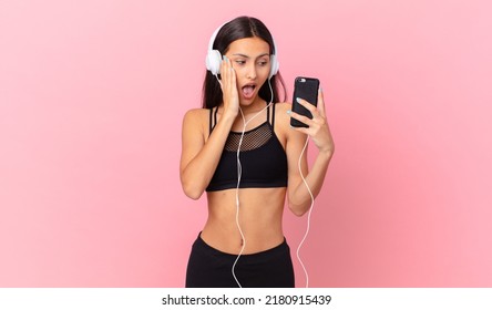 Hispanic Fitness Woman Feeling Happy, Excited And Surprised With Headphones And A Phone