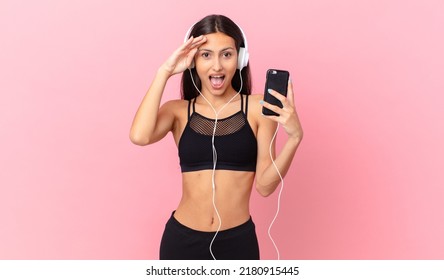 Hispanic Fitness Woman Looking Happy, Astonished And Surprised With Headphones And A Phone