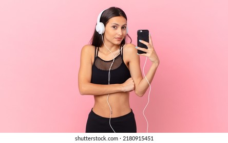 Hispanic Fitness Woman Shrugging, Feeling Confused And Uncertain With Headphones And A Phone