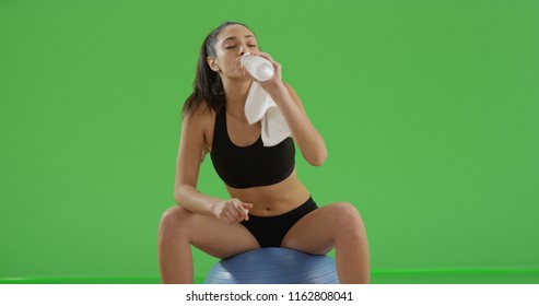 Hispanic Girl Drinking Water Sitting On Exercise Ball On Green Screen