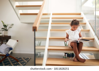 Hispanic Girl Sitting On Staircase In Modern Home Reading Book