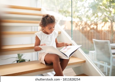 Hispanic Girl Sitting On Staircase In Modern Home Reading Book