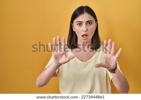 Hispanic girl wearing casual t shirt over yellow background doing stop gesture with hands palms, angry and frustration expression 