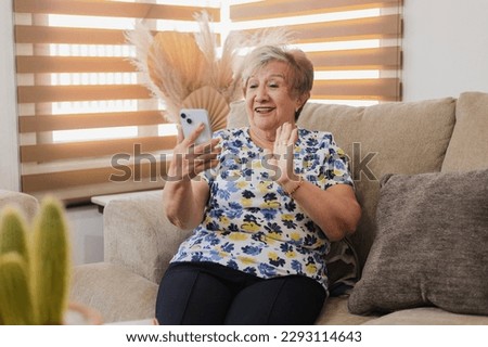 Hispanic grandmother smiling on a video call with her smart phone in her hands-Retired woman smiling holding a smartphone in the living room