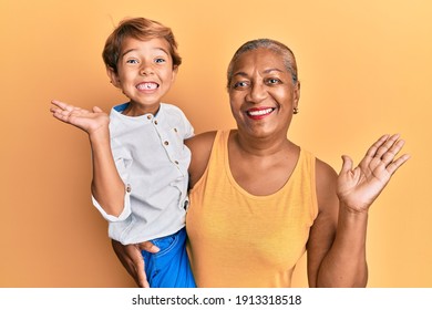 Hispanic Grandson And Grandmother Together Over Yellow Background Celebrating Achievement With Happy Smile And Winner Expression With Raised Hand 