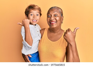 Hispanic Grandson And Grandmother Together Over Yellow Background Pointing Thumb Up To The Side Smiling Happy With Open Mouth 