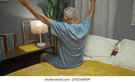 Hispanic grey-haired man waking up in his bedroom stretching on his bed indoors, signifying mornings in a cozy home setting. - Powered by Shutterstock