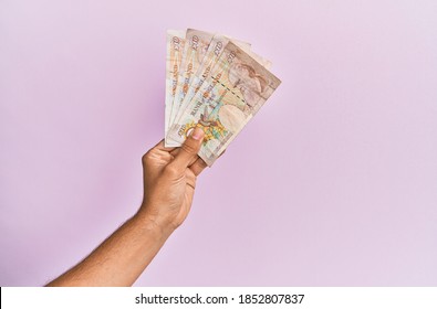Hispanic hand holding 10 uk pounds banknotes over isolated pink background.