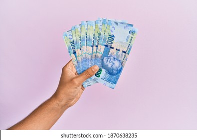 Hispanic hand holding 100 south africa rands banknotes over isolated pink background.