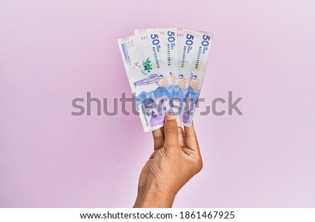 Hispanic hand holding 50 colombian pesos  banknotes over isolated pink background. Foto stock © 