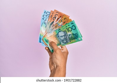 Hispanic hand holding australian dollars banknotes over isolated pink background.