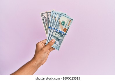 Hispanic hand holding usa dollars banknotes over isolated pink background.