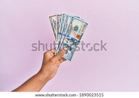 Hispanic hand holding usa dollars banknotes over isolated pink background.