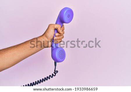 Hispanic hand holding vintage telephone over isolated pink background.