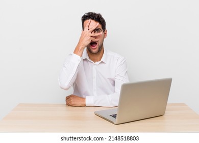 hispanic handsome man looking shocked, scared or terrified, covering face with hand. businessman and desk concept