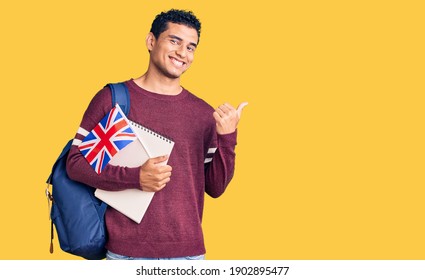 Hispanic handsome young man exchange student holding uk flag pointing thumb up to the side smiling happy with open mouth  - Powered by Shutterstock