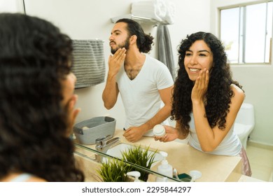 Hispanic happy couple smiling while using skin care products and getting ready in the morning together in the bathroom - Powered by Shutterstock