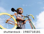 Hispanic hipster carrying a colorful fixie bicycle on his shoulder with a blue sky as background. Sustainable mobility and transport concept.