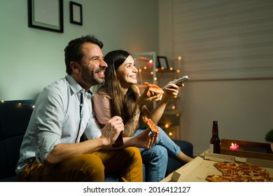 Hispanic Husband And Wife Laughing And Watching A Comedy Movie While Eating Dinner Together For A Chill Casual Date At Home