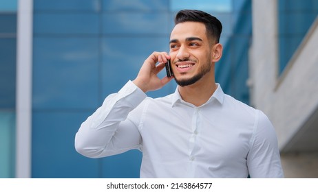 Hispanic indian bearded businessman with mobile phone at street smiling Arabian businessman manager answer call with smartphone outdoors distant communication cheerful guy talking cellphone outside
