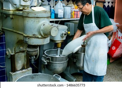 Hispanic Male Blue Collar Worker Is Using An Industrial Stand Mixer To Create Delicious Pastries For His Bakery Shop. The Steel Machine Helps With High-end  Production Of Food For Customers