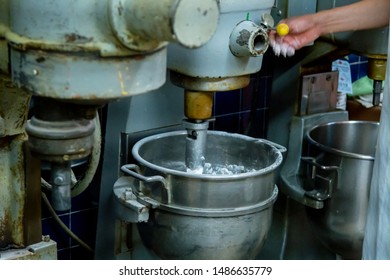 Hispanic Male Blue Collar Worker Is Using An Industrial Stand Mixer To Create Delicious Pastries For His Bakery Shop. The Steel Machine Helps With High-end  Production Of Food For Customers