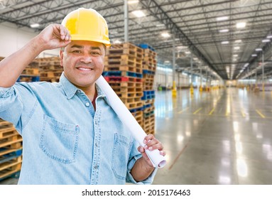 Hispanic Male Contractor Wearing Hard Hat Standing In Empty Industrial Warehouse.