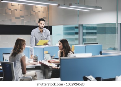 Hispanic Male Employee In Modern Coworking Space, Excluded By Female Colleagues. Adult Businessman In Hostile Working Environment, Holding Files And Trying To Catch Coworkers Attention.