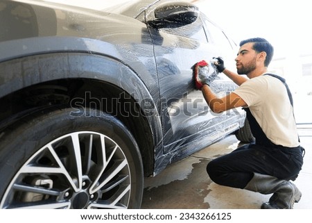 Hispanic male working at car wash washing a customer car with soap and microfiber glove