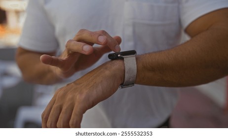 A hispanic man adjusts his smartwatch on an urban street while outdoors, captured in a detailed portrait of his hands and wrist in a city setting. - Powered by Shutterstock