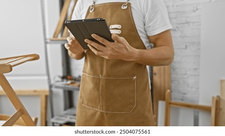 Hispanic man in apron using tablet in carpentry workshop