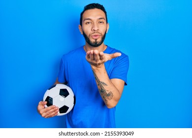 Hispanic man with beard holding soccer ball looking at the camera blowing a kiss with hand on air being lovely and sexy. love expression. 