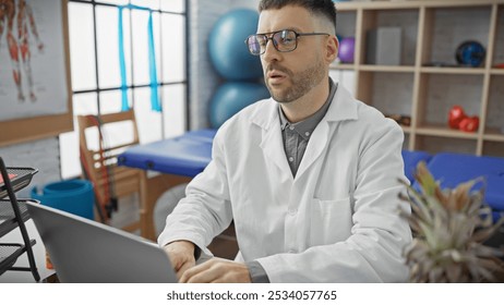 Hispanic man with beard in lab coat working on laptop at rehab clinic. - Powered by Shutterstock