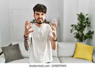 Hispanic Man With Beard At The Living Room At Home Shouting Frustrated With Rage, Hands Trying To Strangle, Yelling Mad 