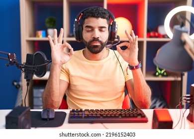 Hispanic Man With Beard Playing Video Games With Headphones Relax And Smiling With Eyes Closed Doing Meditation Gesture With Fingers. Yoga Concept. 