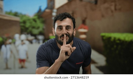 Hispanic man with beard smiling and gesturing silence outdoors on sunny street with blurred background emphasizing tranquility and peaceful atmosphere