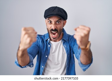 Hispanic man with beard standing over isolated background angry and mad raising fists frustrated and furious while shouting with anger. rage and aggressive concept.  - Shutterstock ID 2177397103