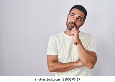 Hispanic man with beard standing over isolated background with hand on chin thinking about question, pensive expression. smiling with thoughtful face. doubt concept.  - Shutterstock ID 2190270417