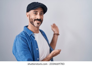 Hispanic man with beard standing over isolated background inviting to enter smiling natural with open hand 