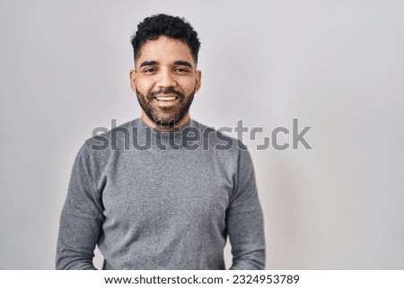 Hispanic man with beard standing over white background with hands together and crossed fingers smiling relaxed and cheerful. success and optimistic 